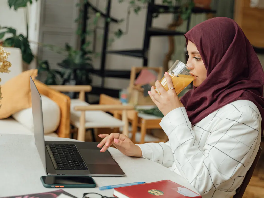 A woman drinking juice while responding to emails