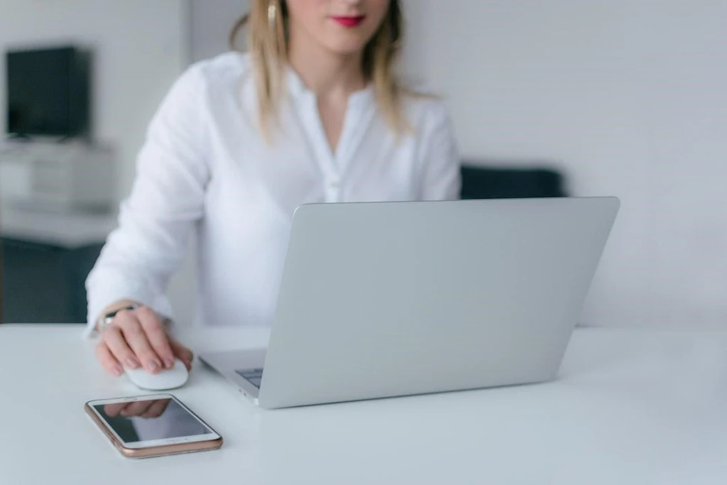 A woman working using a laptop with a cellphone beside it.